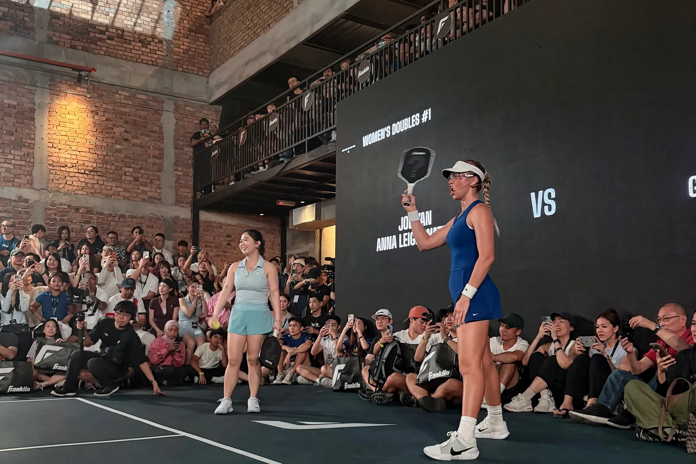 Anna Leigh Waters stands ready with her paddle raised, with another player behind her and the women’s doubles scoreboard on the screen