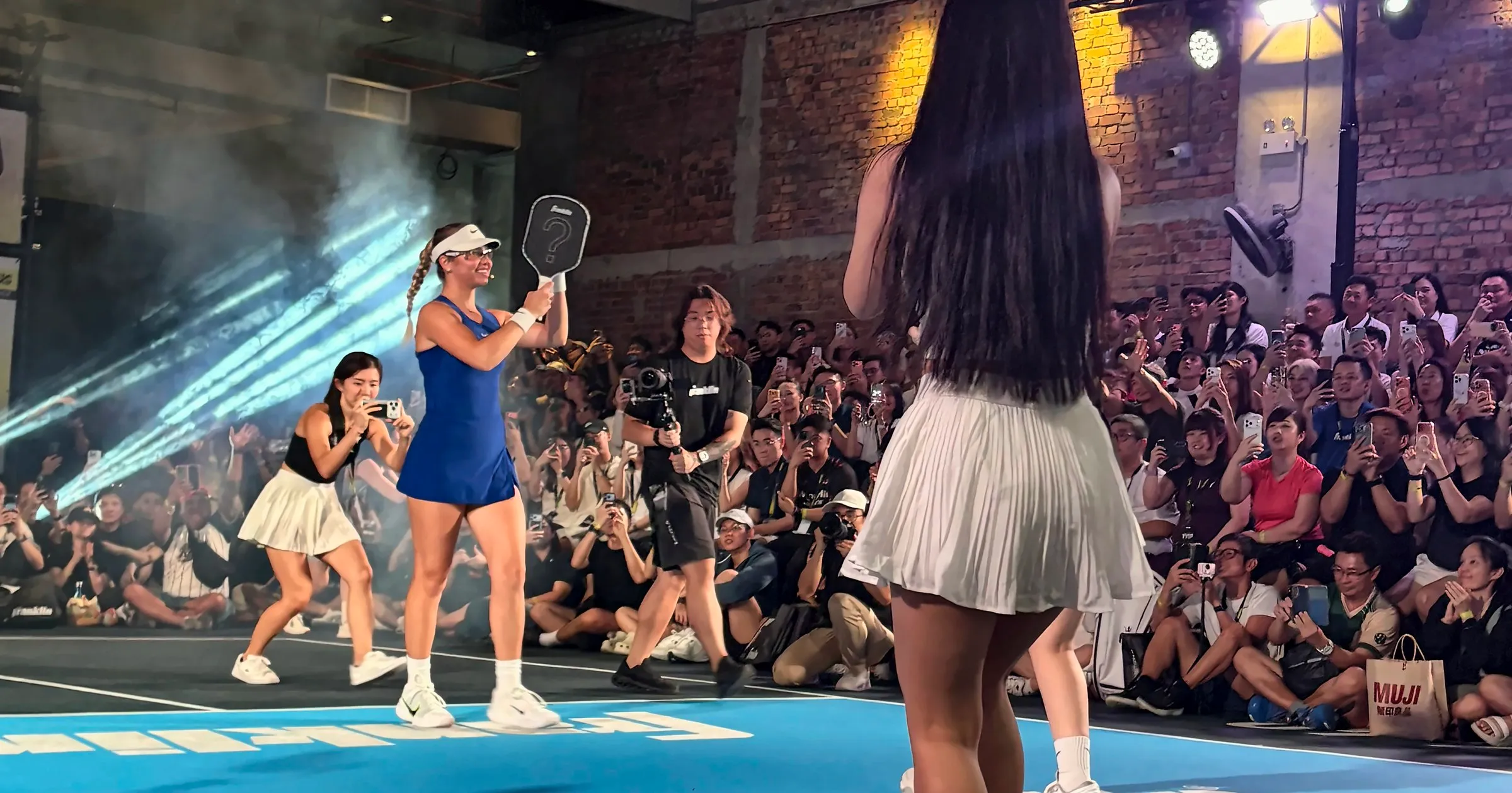 Anna Leigh Waters walks out through stage smoke holding up a paddle, as the crowd on the sideline films her