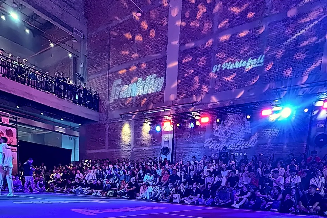 A wide view of the court under blue light, with the crowd seated along the far wall beneath the Franklin and 91 Pickleball projections