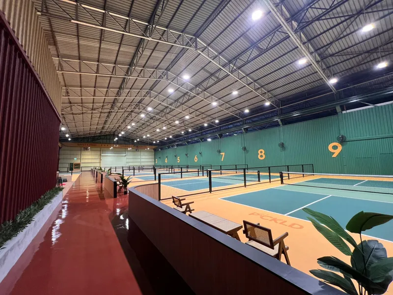 Indoor hall with rows of numbered pickleball courts in teal and orange under a steel roof at PICKLD.