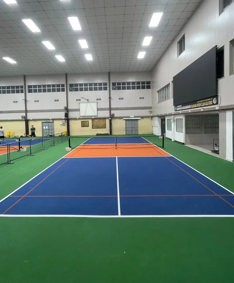 Indoor hall with blue, orange and green pickleball courts under a high ceiling