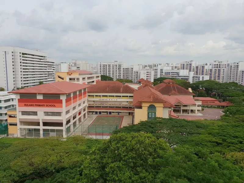 Elevated view of Rulang Primary School's red-roofed buildings, one marked "Rulang Primary School", with an outdoor court and HDB blocks behind.