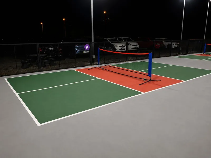 Floodlit outdoor pickleball courts at night with a net and perimeter fence