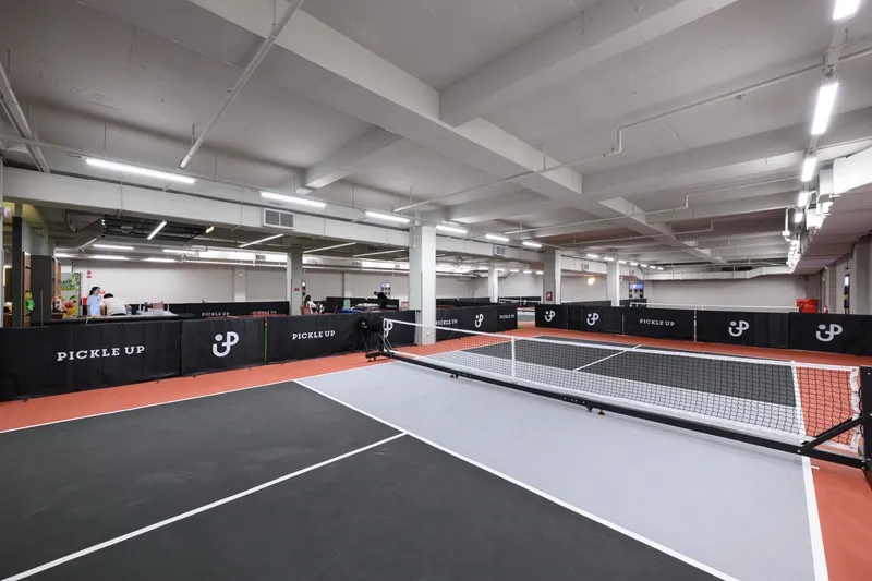 Indoor air-conditioned pickleball courts with grey and black surfaces and Pickle Up branded barriers at Pickle Up @ OCC, Orchid Country Club