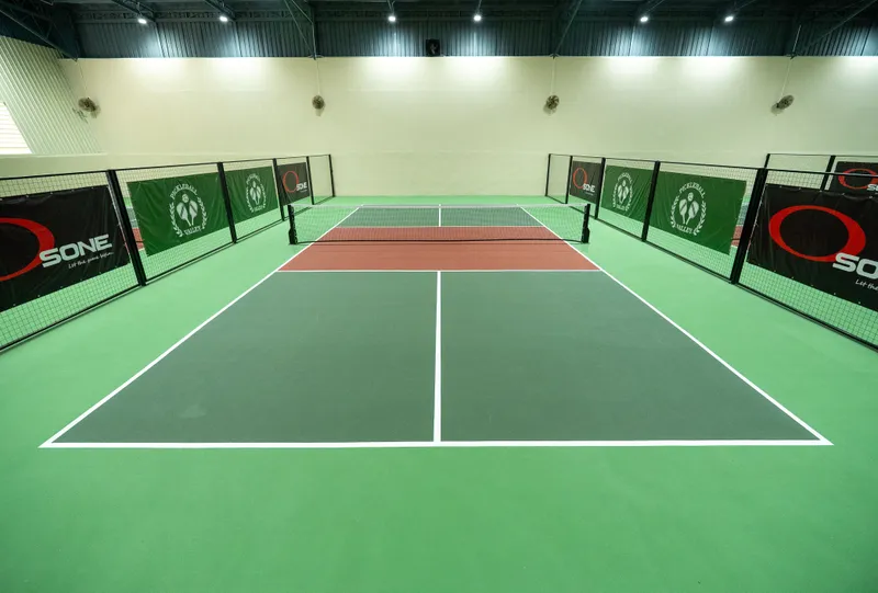 Indoor pickleball court with green surround, net and Pickleball Valley banners on the side fencing