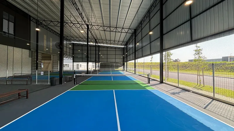 Covered blue and green pickleball courts with nets under a steel-roofed hall at Seven Fit Sports Centre