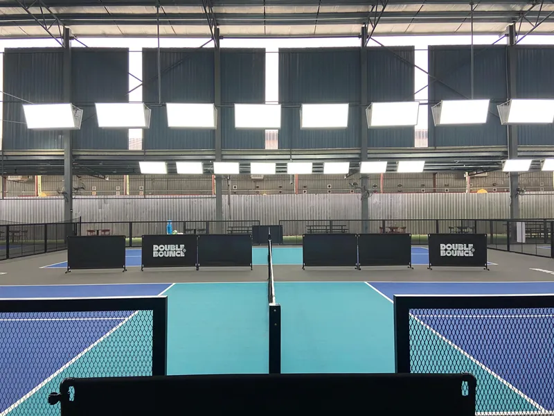Indoor pickleball courts in blue and teal at Double Bounce Balakong, with Double Bounce branded court dividers