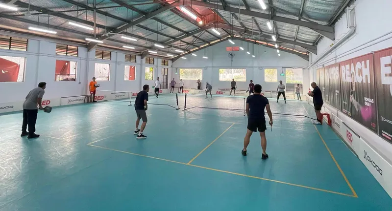 Players in doubles games on the teal indoor pickleball courts under the high steel roof at RED Quarters in Kallang