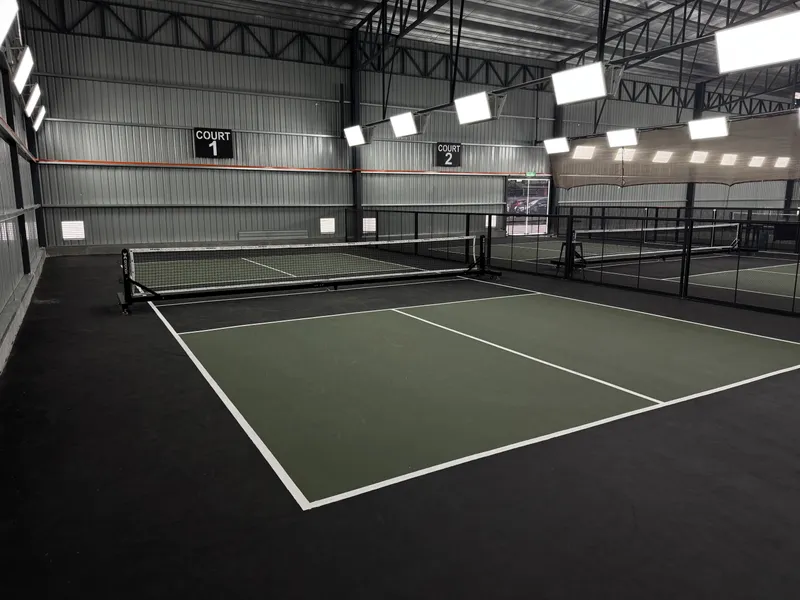 Indoor pickleball hall at Apex Pickleball, Ampang, with green courts on a dark floor, permanent nets, Court 1 and Court 2 signs and LED lights under a steel roof