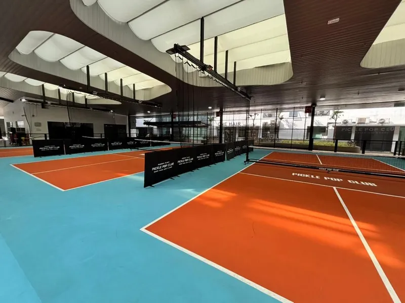 Covered orange pickleball courts with turquoise surrounds and Pickle Pop Club branded barriers under a white fabric canopy at Aurora Place, Bukit Jalil