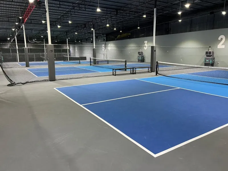 Indoor pickleball hall with several blue courts, nets and numbered walls under a dark ceiling