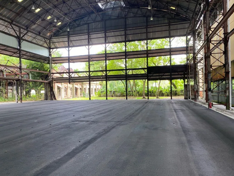 The open-sided steel-framed shed at Sentul Depot that houses PickleDepot, shown with a bare floor before the courts were laid, with trees and old depot buildings behind