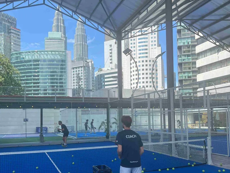 Rooftop courts at Padel Bintang on Wisma Cosway, with a covered padel court in front, pickleball courts behind glass and the Petronas Twin Towers beyond