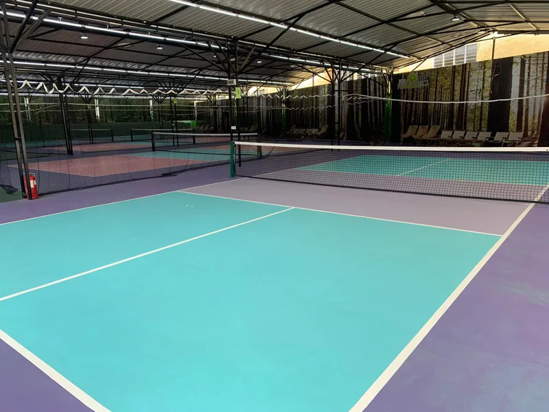 Covered pickleball courts at Ecosega Pickleball Park with teal and lilac surfaces, nets, a steel roof with LED lighting, and forest-print wall banners